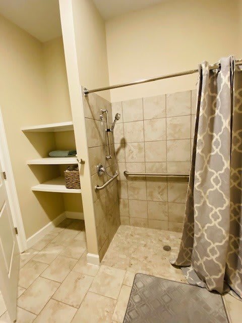A bathroom featuring a tiled shower with a patterned curtain and nearby shelving.