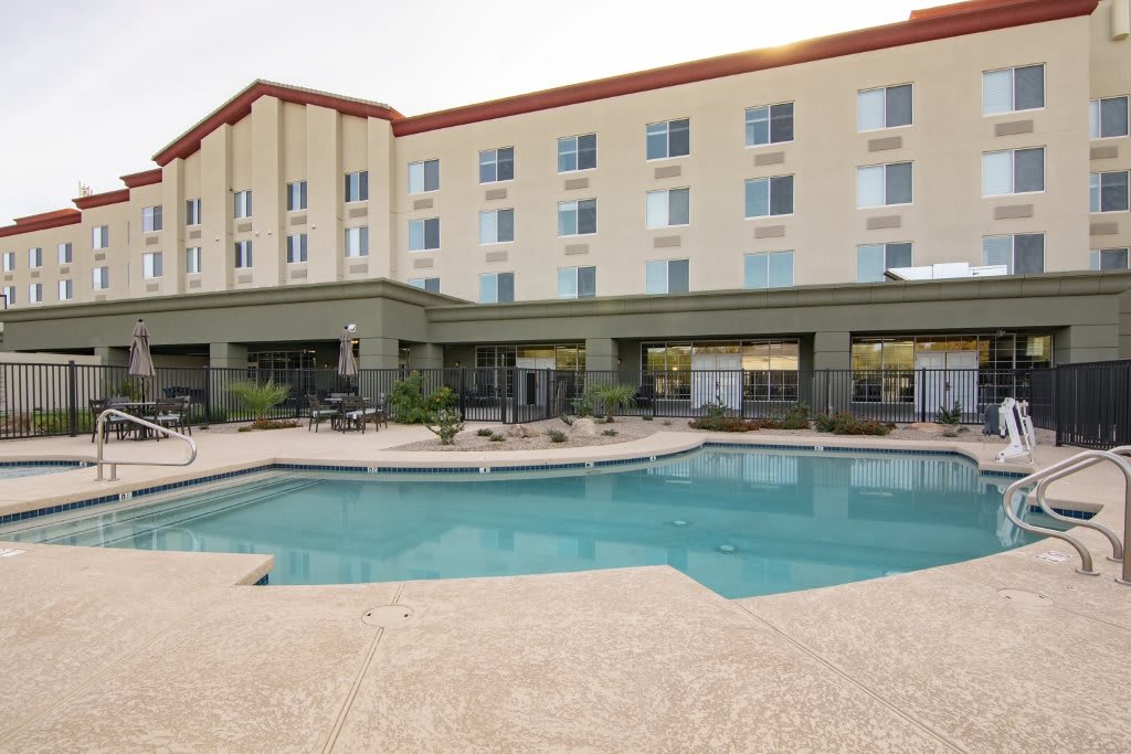An outdoor pool area at a hotel with a multi-story building in the background.