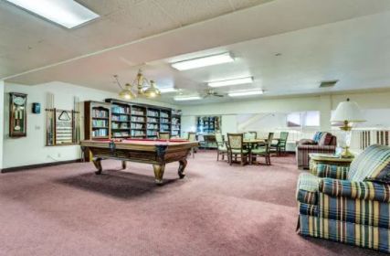 A spacious recreational room featuring a pool table and library shelves, with ample seating and warm lighting.