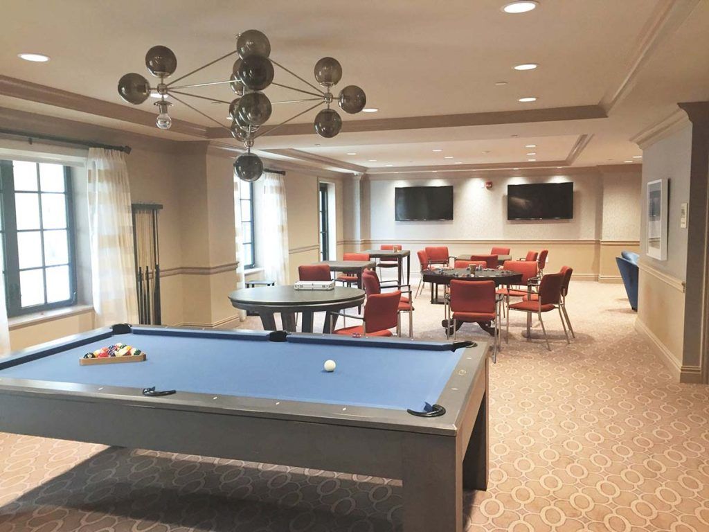 A modern game room featuring a pool table, multiple TVs, and comfortable seating.