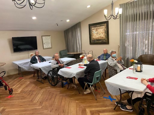 A group of seniors gathered in a cozy indoor setting, engaging in conversation at their tables.
