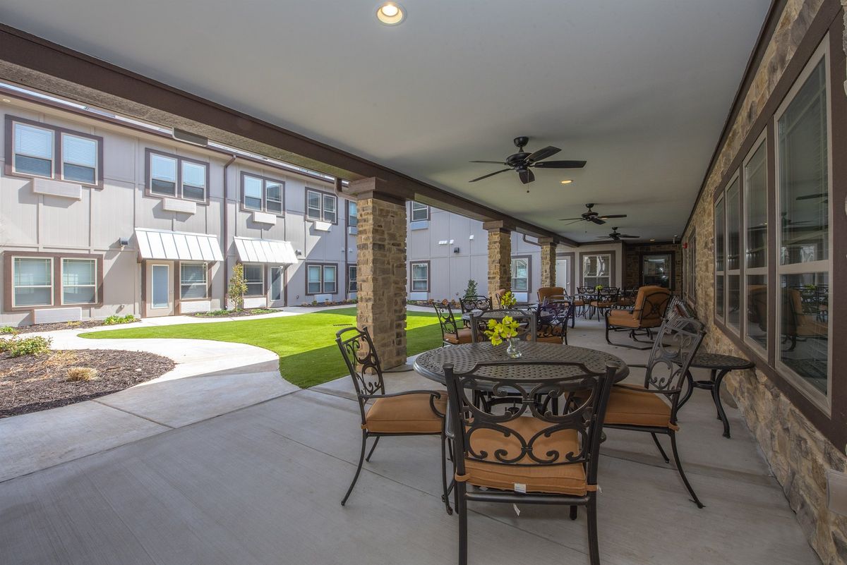 A covered outdoor patio area with seating, overlooking a landscaped garden and building exterior.