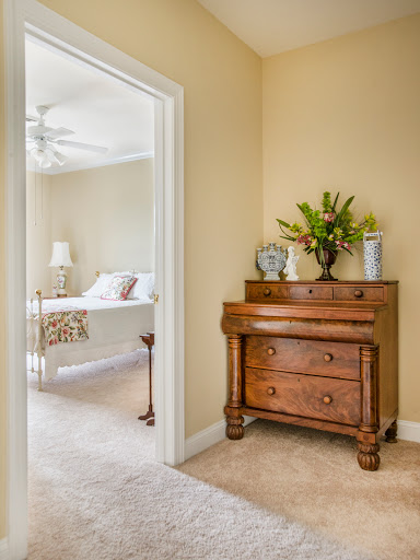 A cozy corner of a bedroom showcasing a wooden dresser adorned with flowers, leading to a softly lit sleeping area.