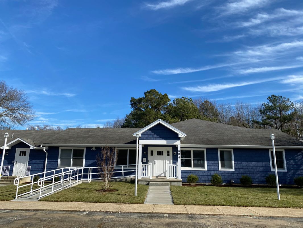 A single-story blue house with a front porch and ramp set against a bright blue sky.