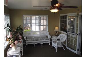 A cozy sunroom featuring wicker furniture and a ceiling fan, with natural light streaming in through the windows.