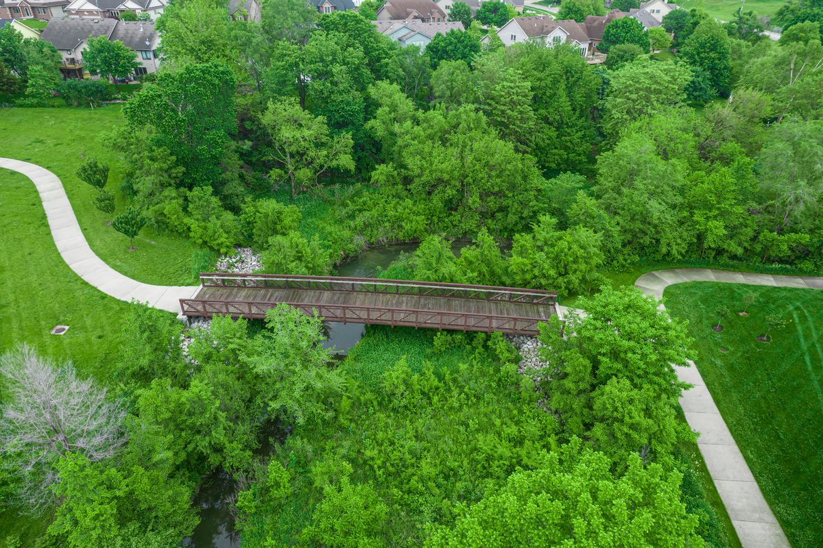 Aerial view of a park featuring a wooden bridge surrounded by lush greenery and winding pathways.