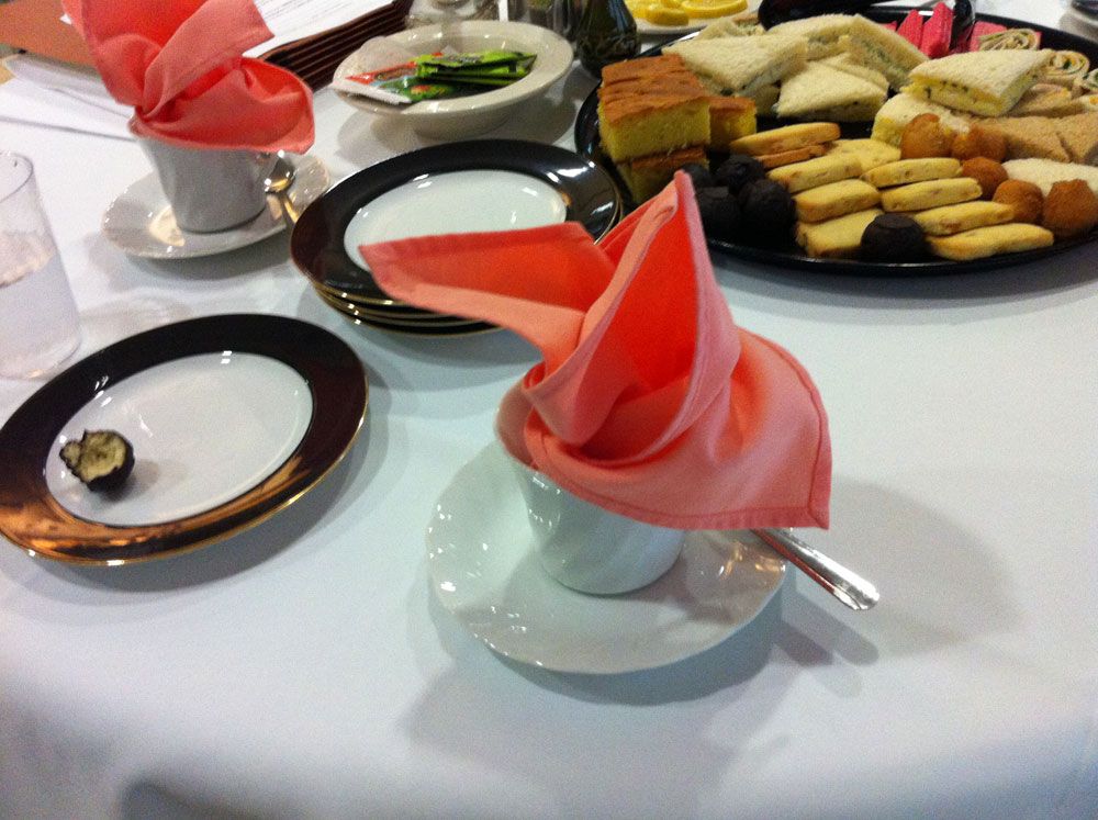A table set with tea cups adorned with folded napkins, accompanied by an assortment of pastries and snacks.