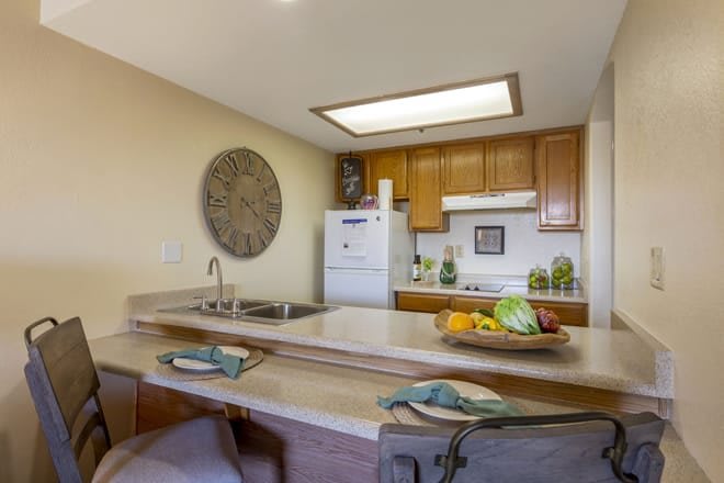 A cozy kitchen with wooden cabinets and a countertop, featuring a sink, stove, and decorative wall art.