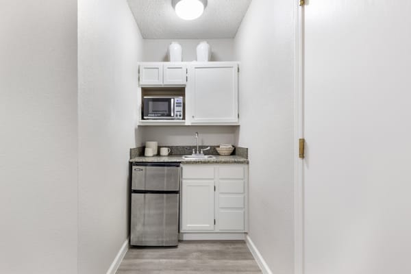 A compact kitchen area with white cabinetry, a microwave, and a mini fridge.