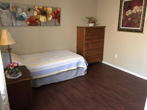 A simple and clean bedroom setup featuring a bed with a light blanket, a wooden dresser, and decorative artwork on the wall.
