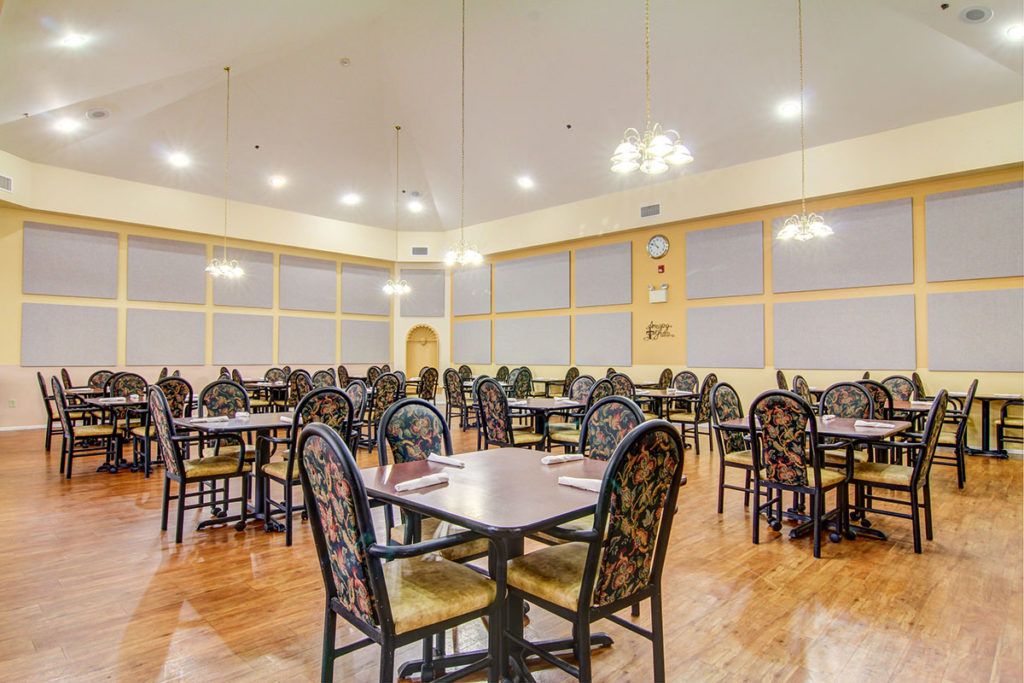 An empty dining room with neatly arranged tables and chairs, illuminated by overhead lighting.