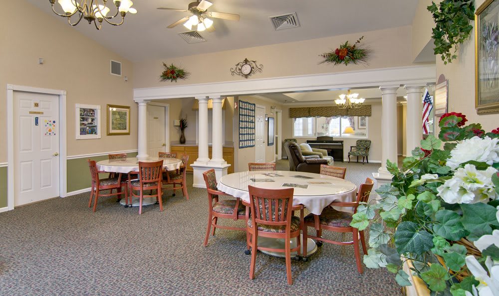 A traditionally styled dining area with multiple round tables and chairs, decorated with plants and lighting fixtures.