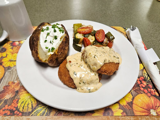 A delicious dinner plate featuring baked potato with sour cream, fried items topped with gravy, and a side of mixed vegetables.