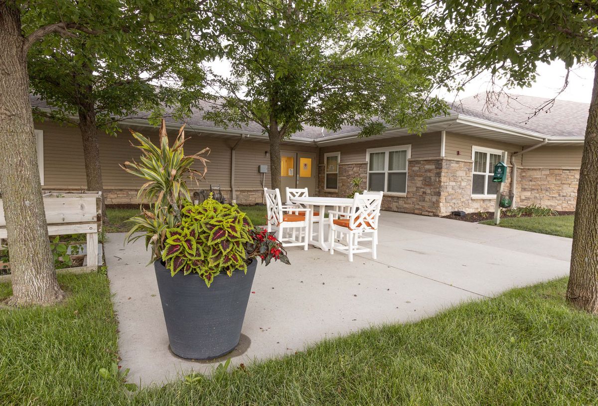 A cozy outdoor patio with white furniture, surrounded by greenery and a large potted plant.