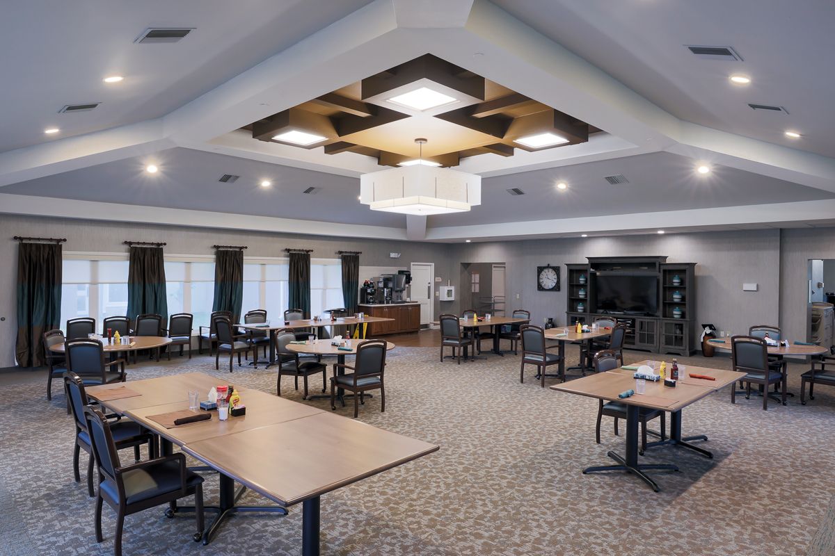 A spacious and modern conference room with multiple tables and chairs arranged for meetings, featuring a large chandelier and carpeted flooring.