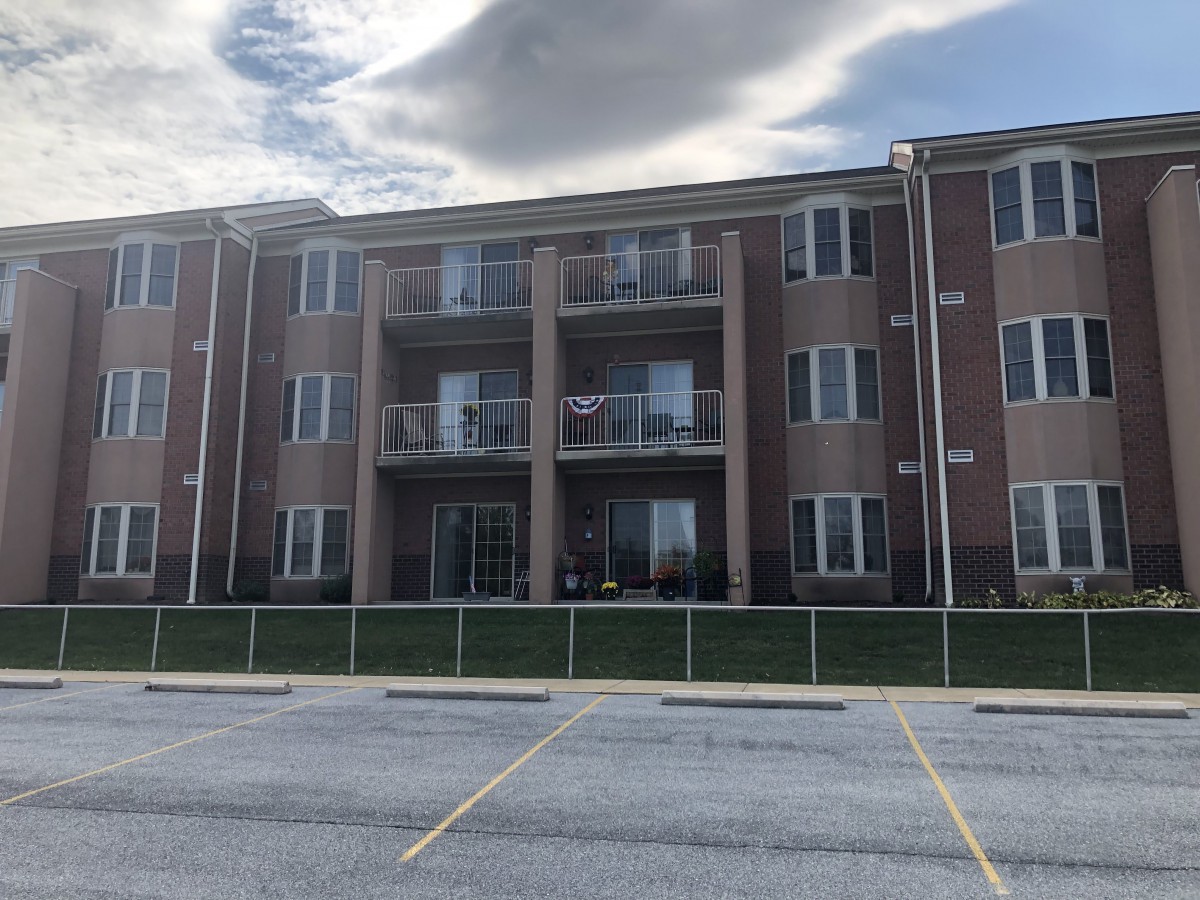 A three-story apartment building with balconies and a parking lot in front.
