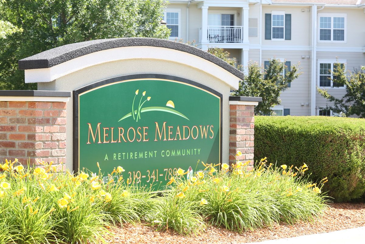 Sign for Melrose Meadows Retirement Community in front of landscaped greenery and residential buildings.