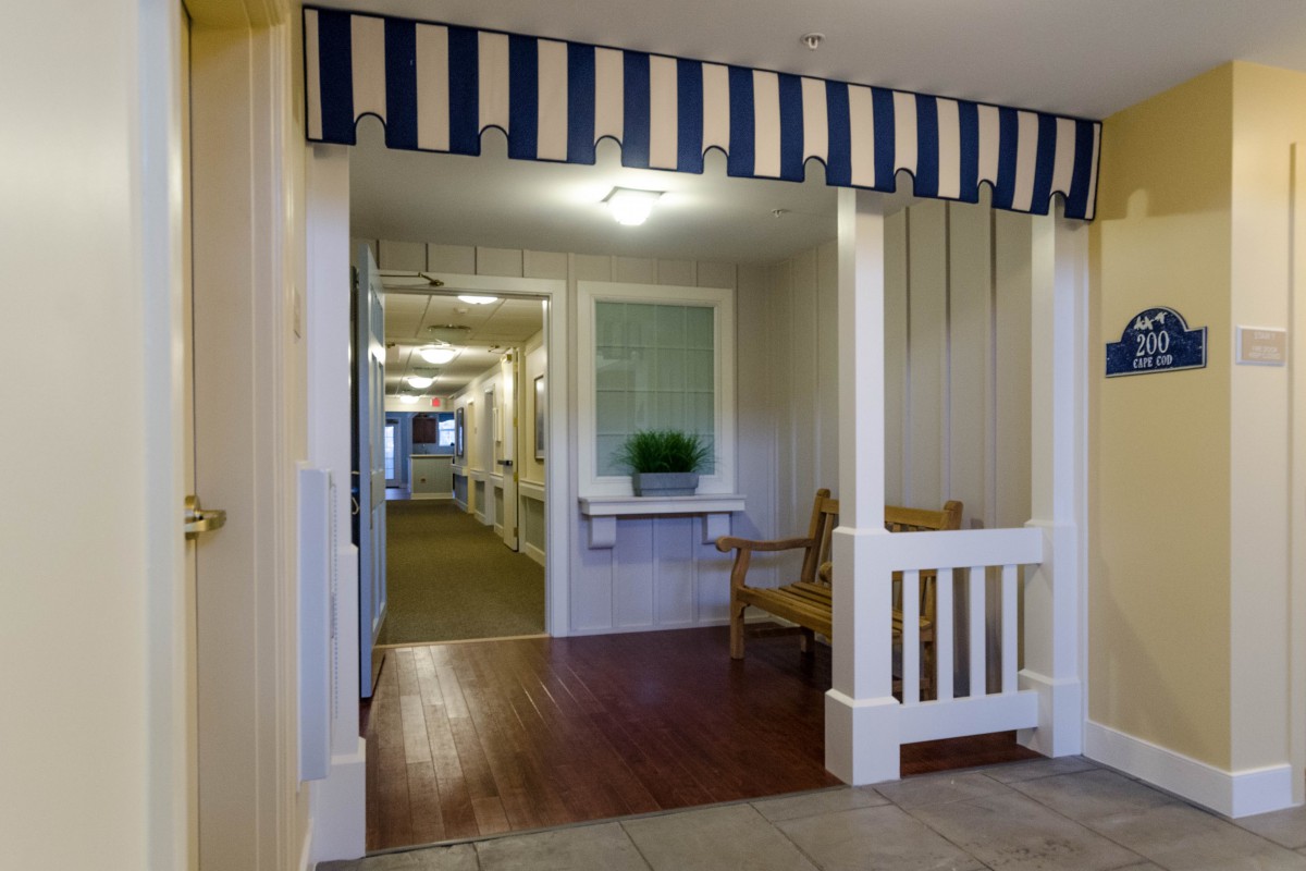 A well-lit hallway with a striped awning and wooden flooring, featuring a bench and window.