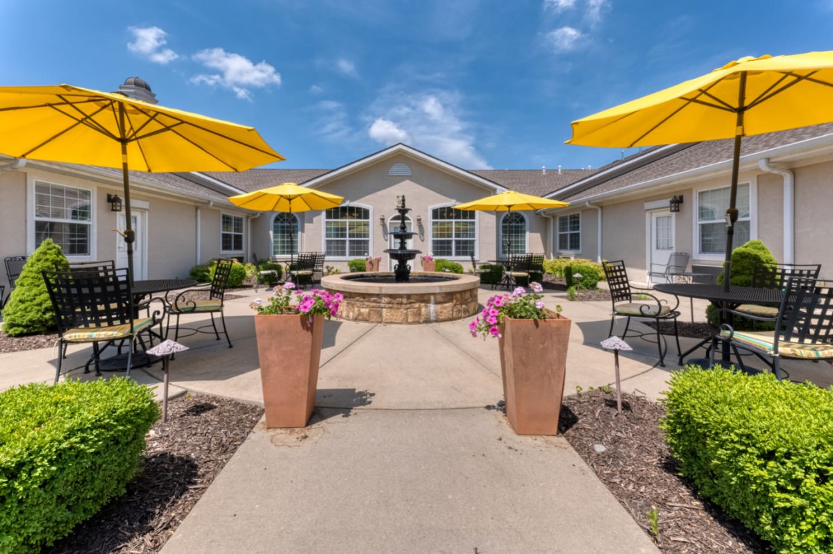 A sunny courtyard with a central fountain, surrounded by outdoor seating and bright yellow umbrellas.