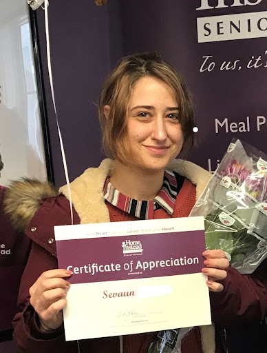 A young woman proudly holding her Certificate of Appreciation, accompanied by flowers.
