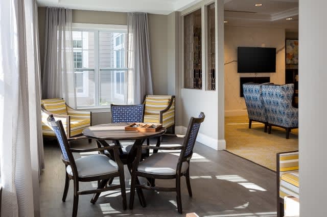A cozy living room with a central round table surrounded by chairs, adjacent to a television area.