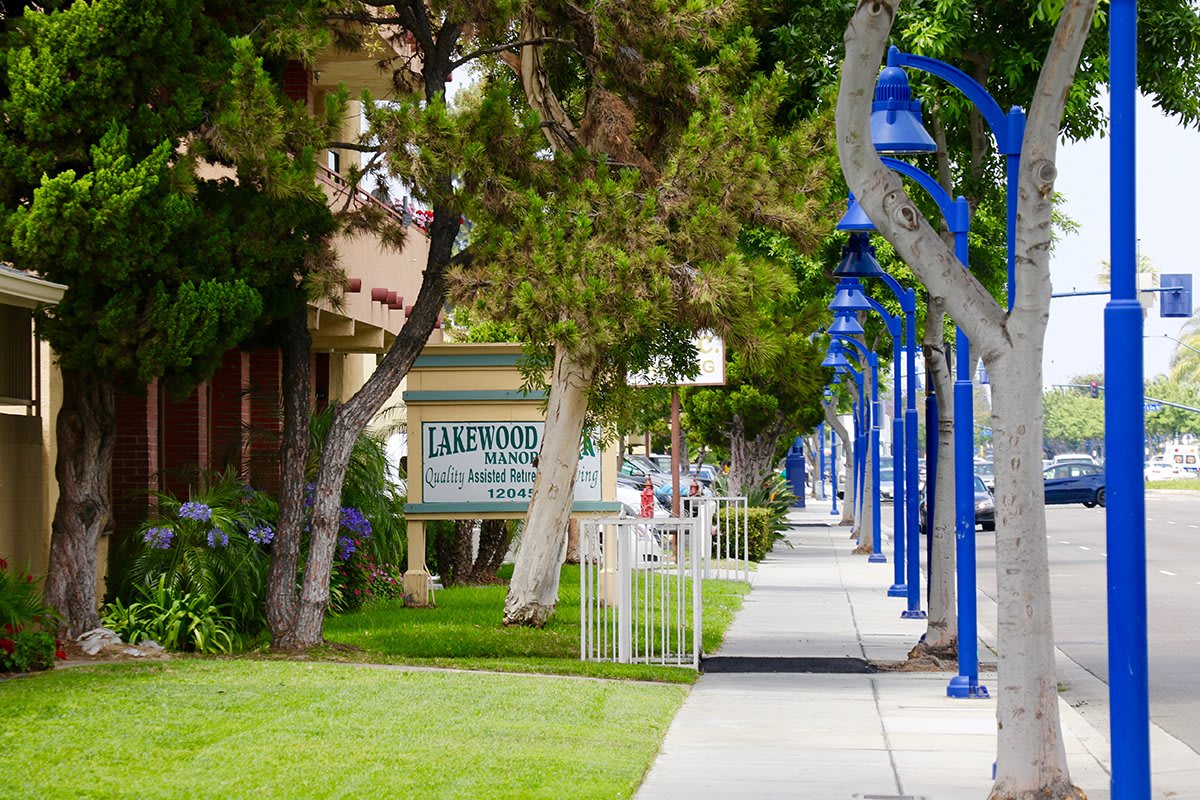 A tree-lined sidewalk with blue street lamps and a signboard in a suburban area.