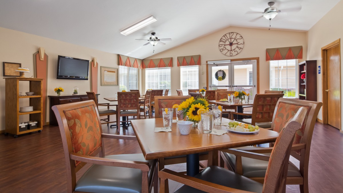 A cozy dining room with wooden tables, chairs, and sunflower centerpieces.