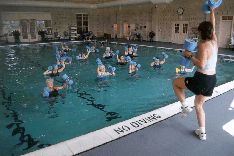 A group of people participating in a water aerobics class in an indoor swimming pool.