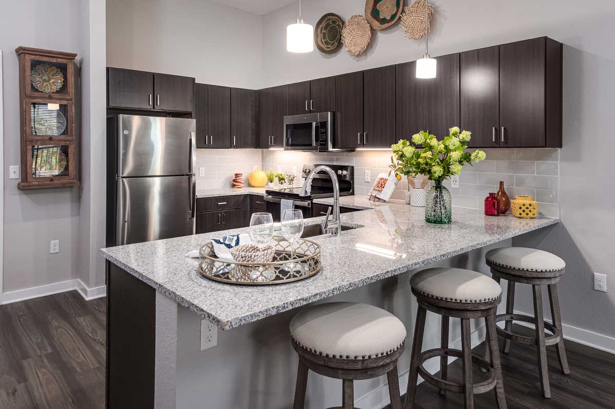 A modern kitchen with stainless steel appliances, a spacious island countertop, and stylish bar stools, adorned with decorative items and flowers.