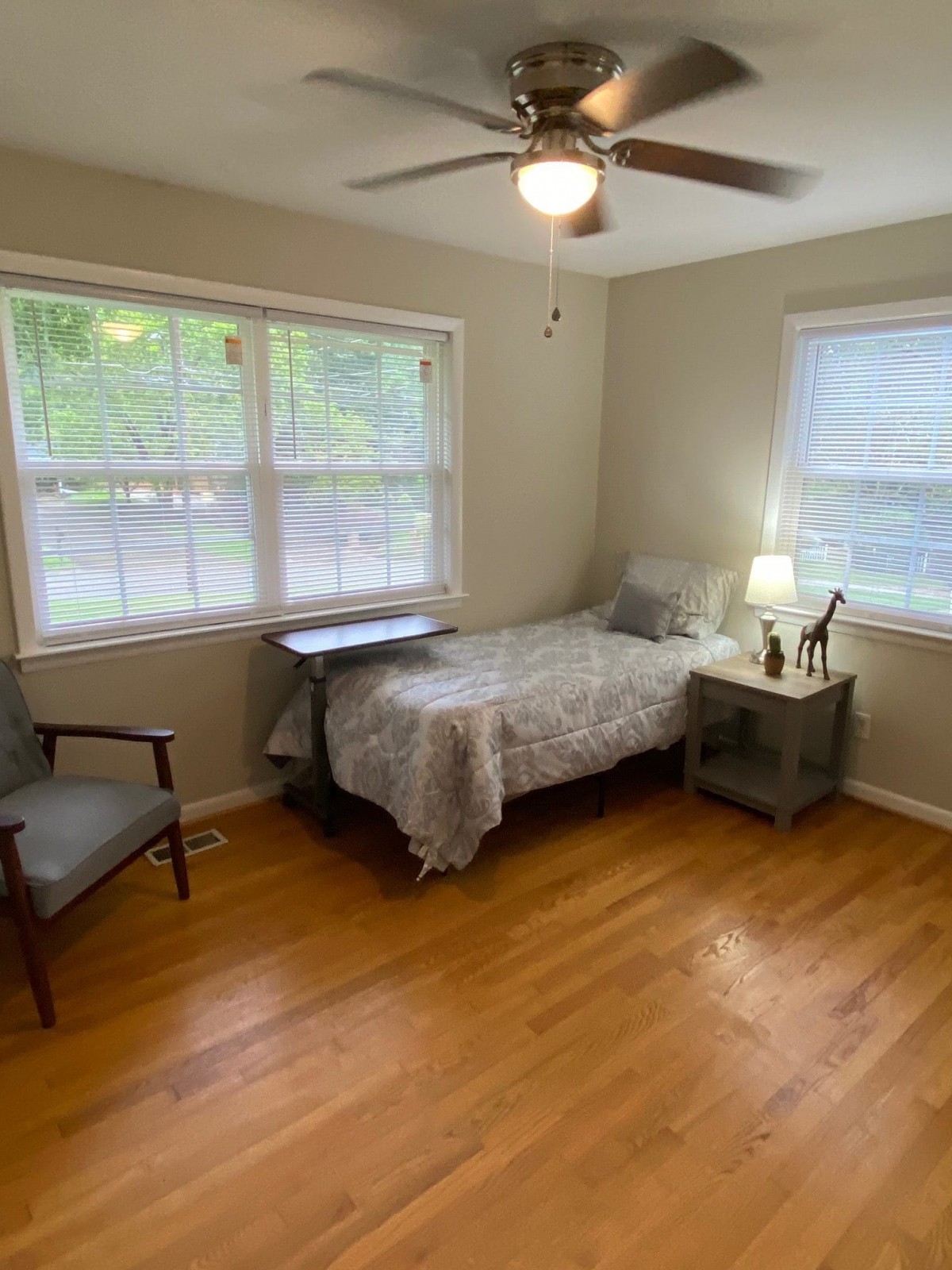 A cozy bedroom with a single bed, chair, and nightstand by the window.