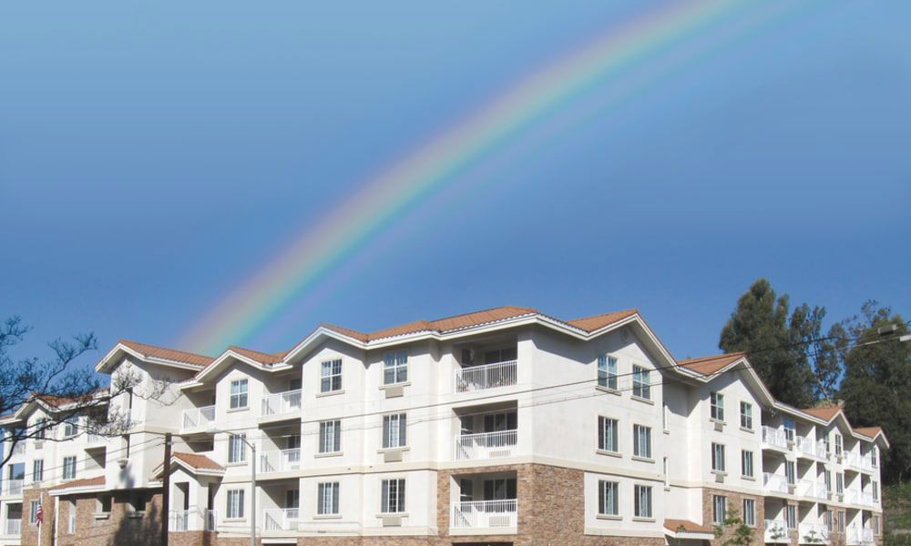 A vibrant rainbow arcs over a modern apartment building under a clear blue sky.
