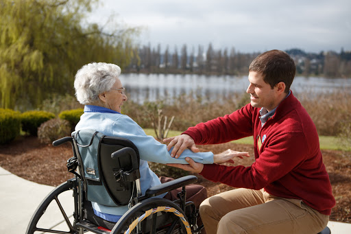 A caregiver assisting an elderly woman in a wheelchair by the lakeside.