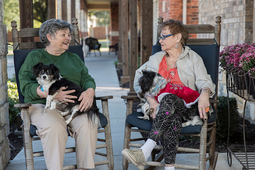 Two elderly women enjoying a conversation on the porch while holding their dogs.
