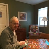 An elderly man working on a puzzle at a table in a cozy room.