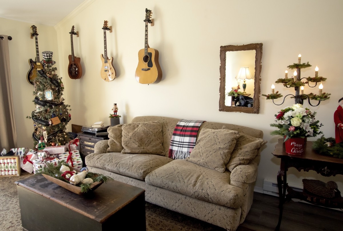 A cozy living room featuring a sofa adorned with a holiday-themed pillow, guitars mounted on the wall, and a decorated Christmas tree adding festive charm.