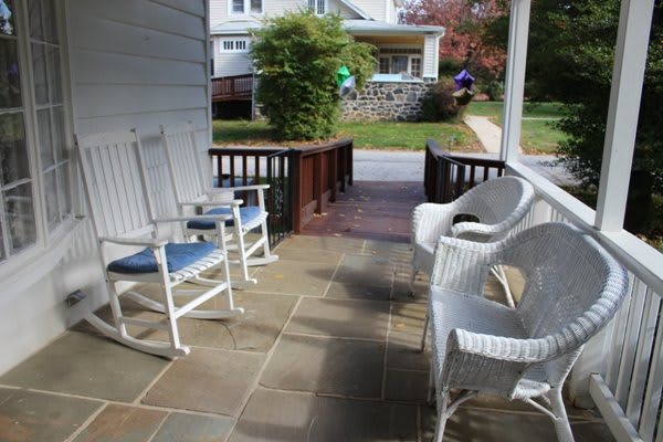 A cozy front porch with white rocking and wicker chairs overlooking a suburban neighborhood.