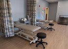 A healthcare examination room with multiple examination tables and stools, separated by curtains.