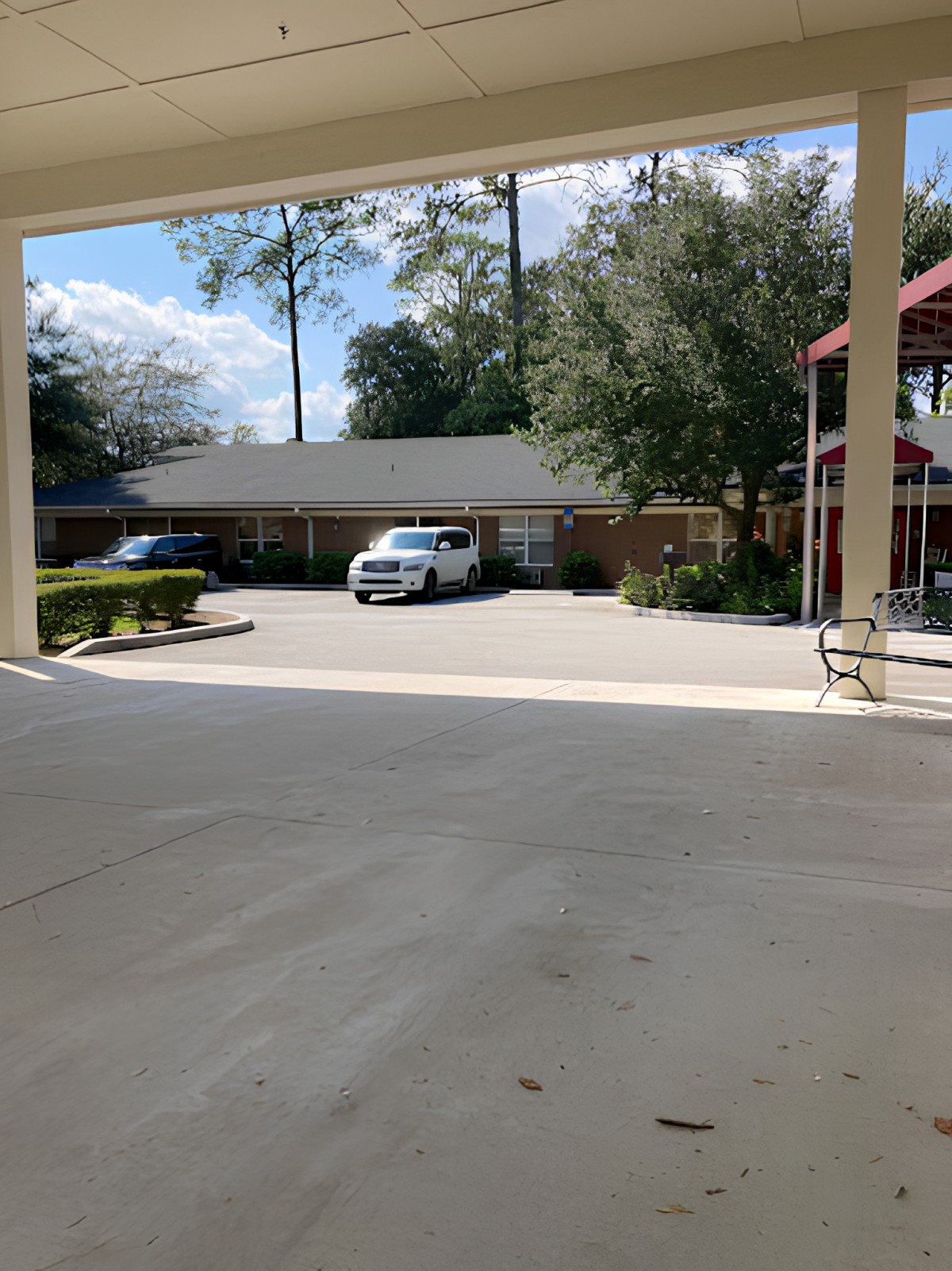 A small parking lot with parked cars in front of a building surrounded by trees on a sunny day.