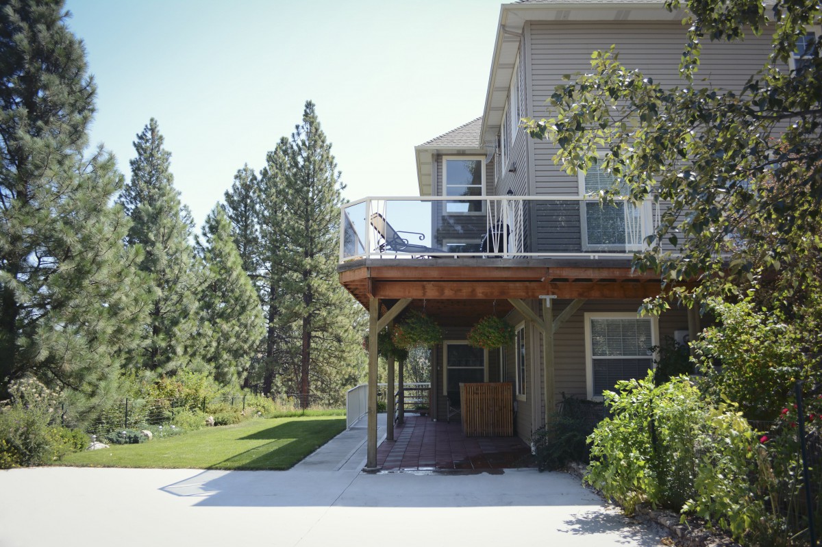 A house with a deck overlooking a lush green lawn and surrounded by trees.