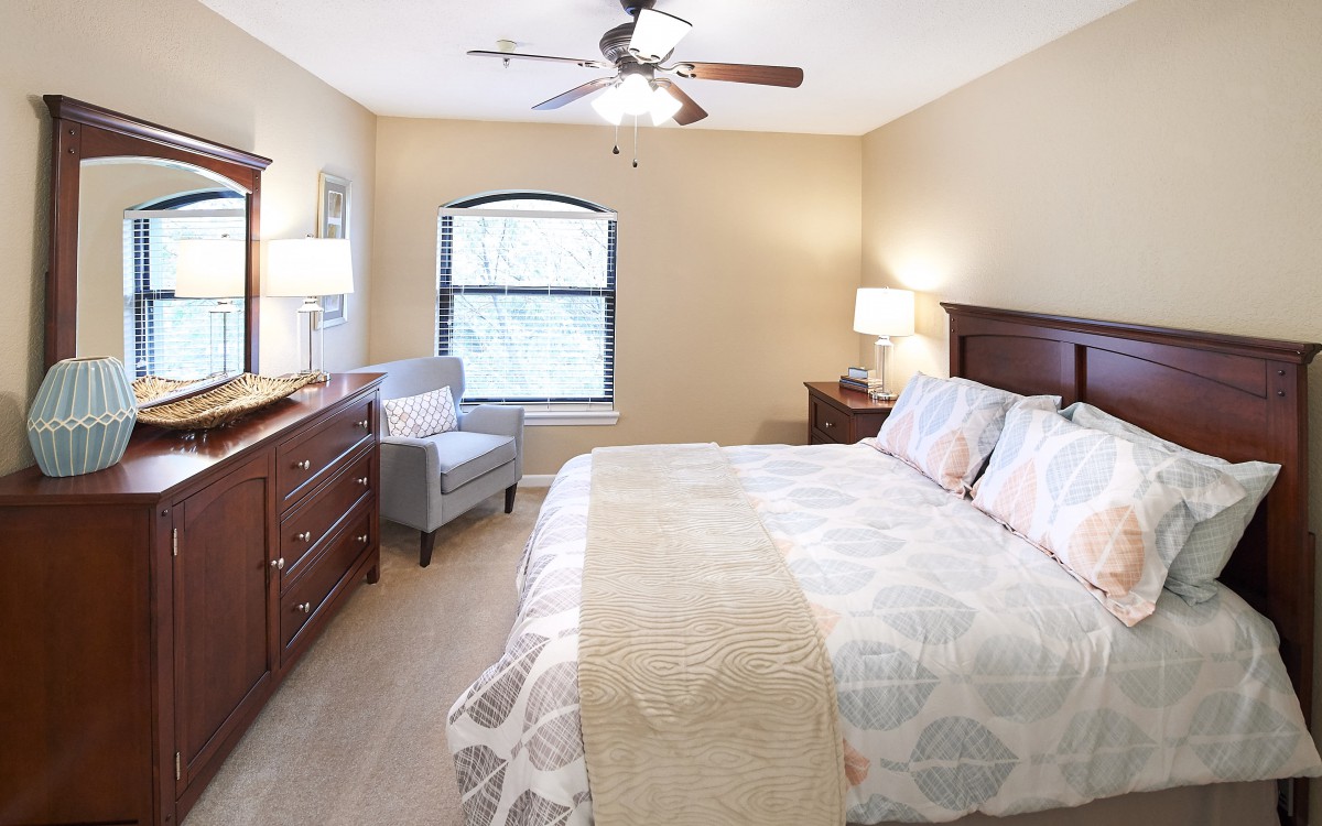 A cozy bedroom with a neatly made bed, wooden furniture, and soft lighting.