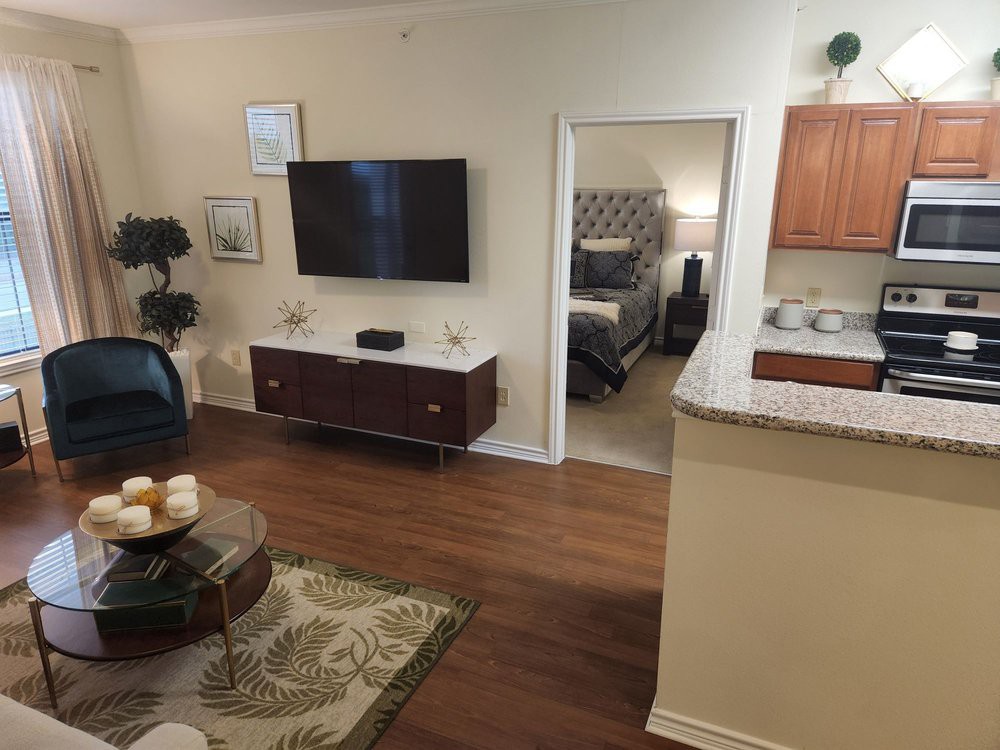 A cozy living space featuring a wall-mounted television, stylish furniture, and an open view into a bedroom and kitchen.
