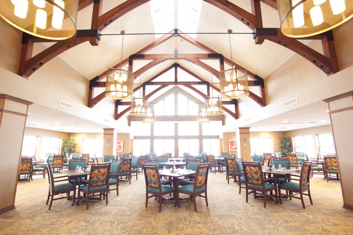 A spacious dining area with elegant wooden beams and large windows, featuring neatly arranged tables and chairs.