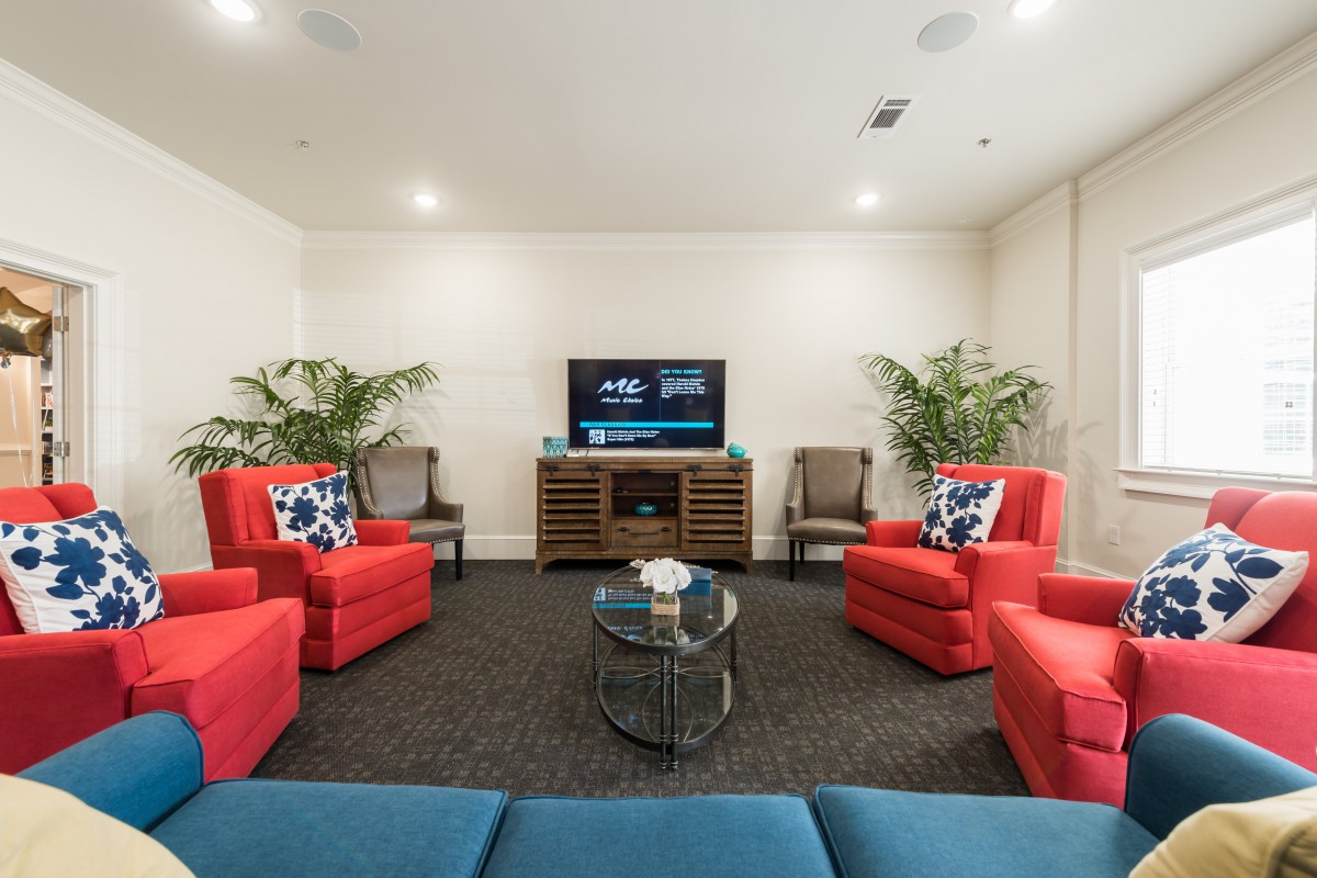 A modern living room with red chairs, a sofa, and a TV, complemented by plants and a central coffee table.