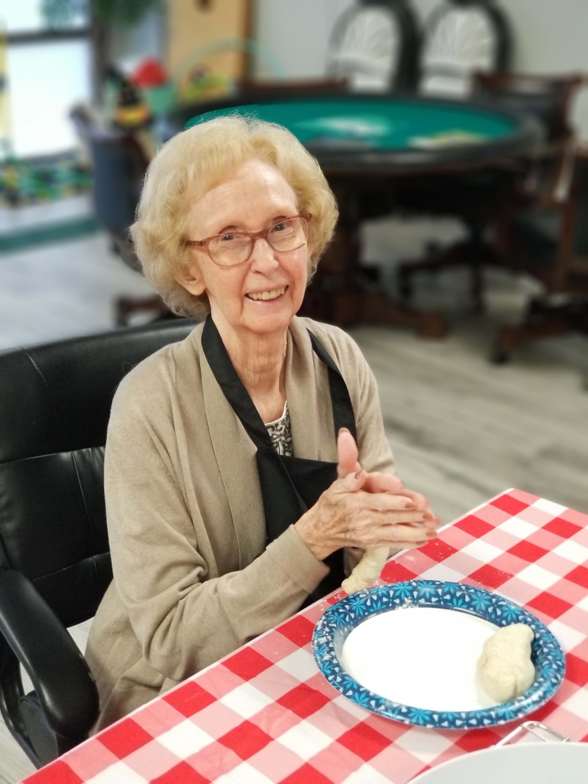 An elderly woman sitting at a table with a checkered tablecloth, preparing to dine.