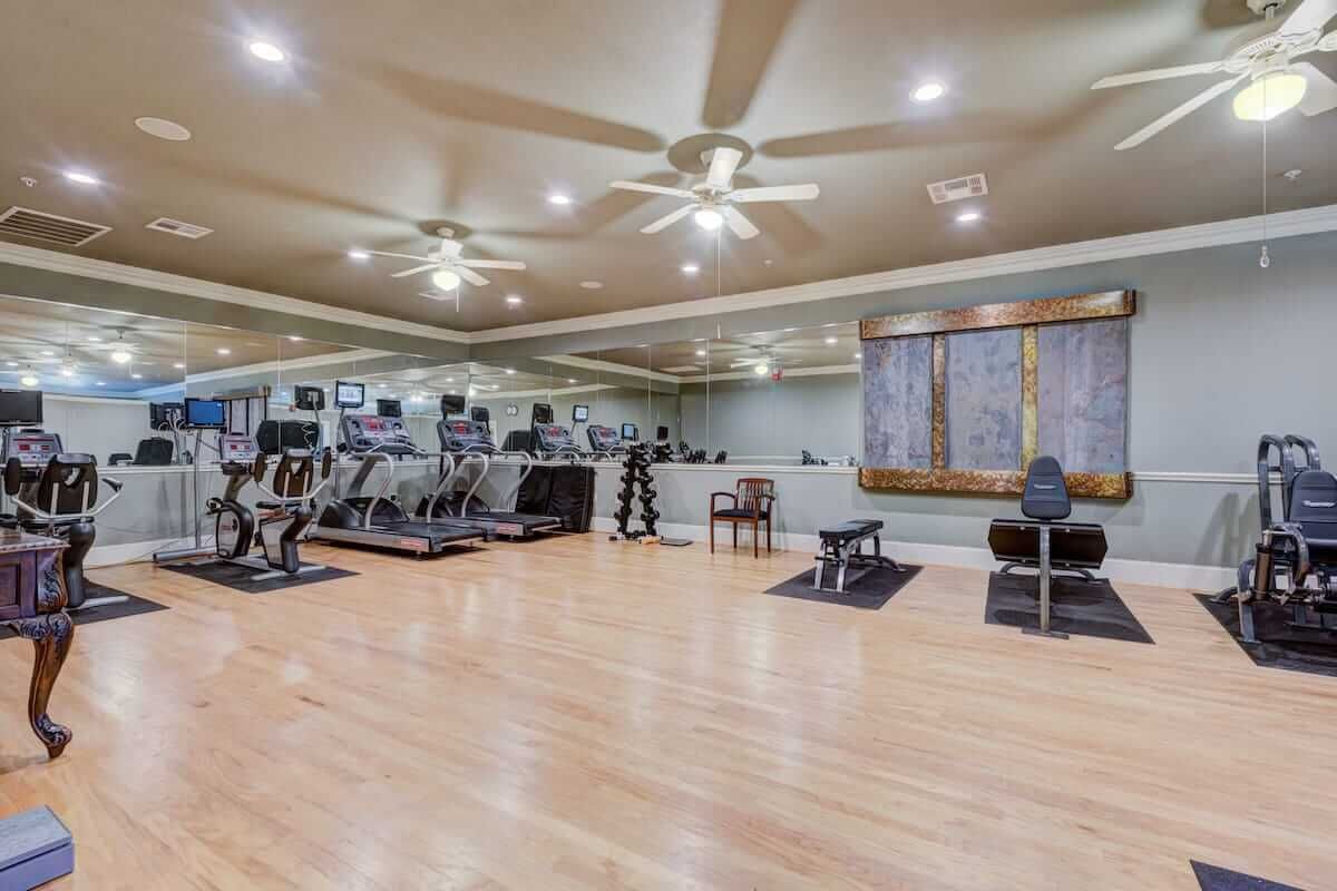 A spacious gym with modern exercise equipment and wooden flooring.
