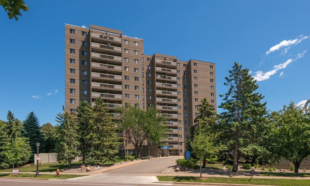 A tall residential apartment building surrounded by trees under a clear blue sky.