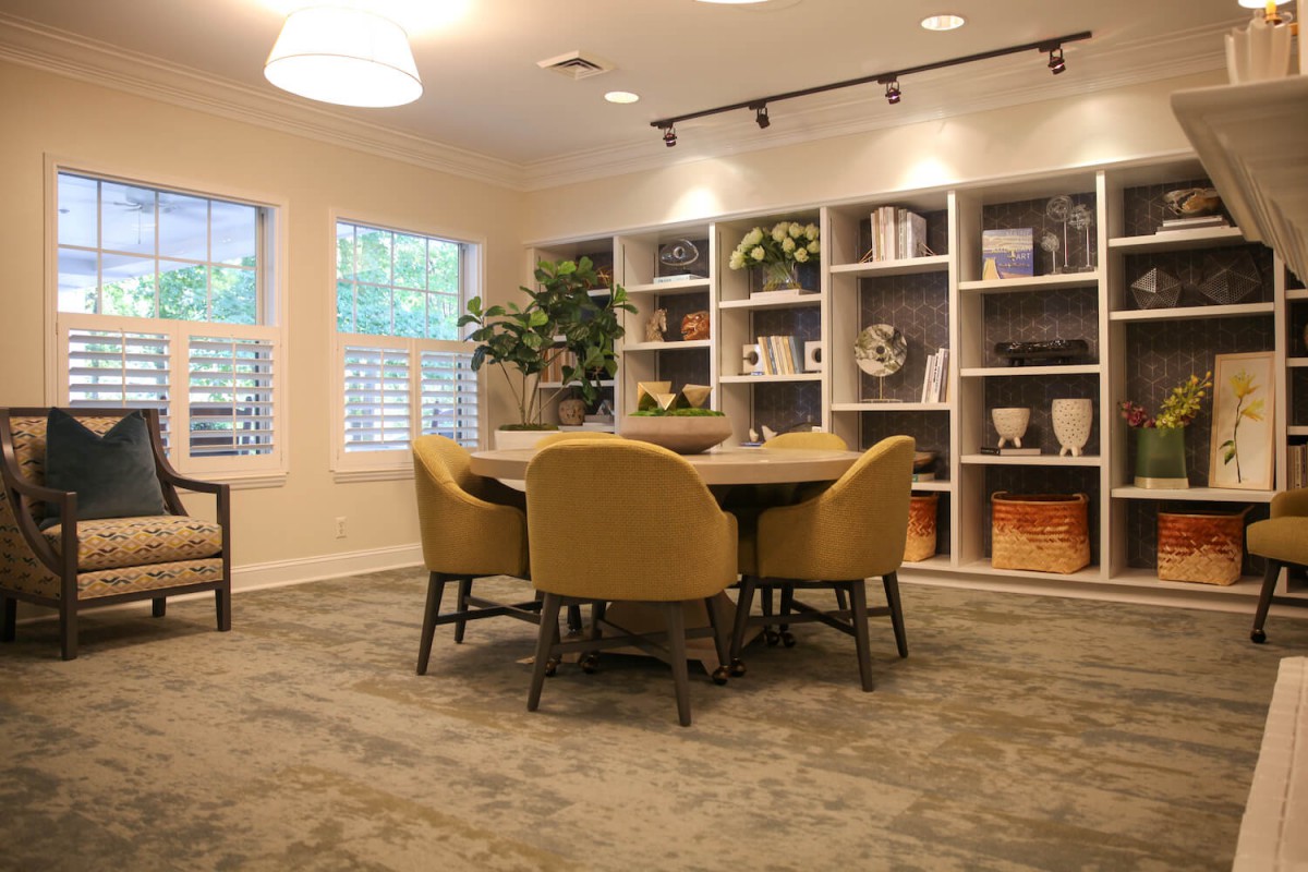 A modern meeting room with a round table and comfortable chairs surrounded by bookshelves and decor.