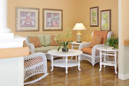 A cozy living room with rattan furniture, featuring a sofa and chairs, a round coffee table, decorative wall art, and an indoor plant.