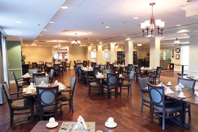 An elegantly furnished restaurant dining room with neatly arranged tables and chairs, featuring warm lighting.