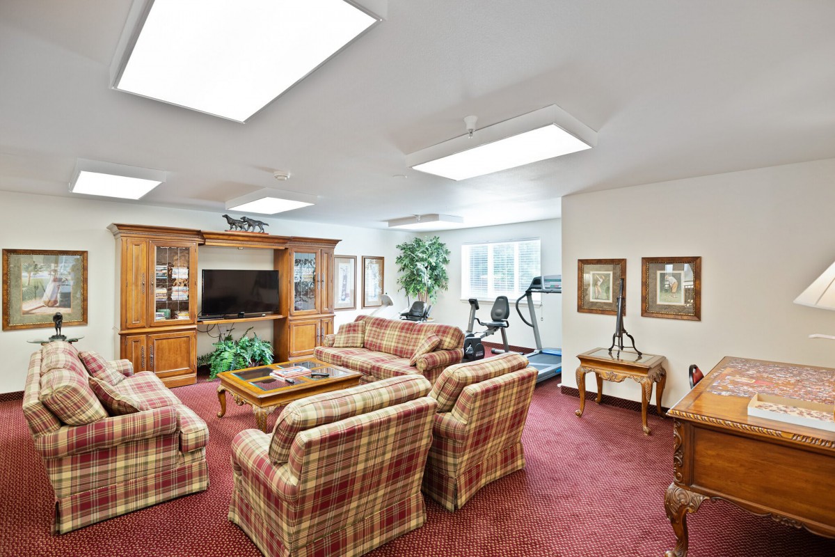 A cozy living room featuring plaid sofas, a large entertainment center with a television, and exercise equipment in the corner.